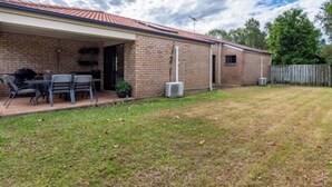 A brick house with a covered patio, a barbecue grill, and a fenced yard. - Sandstone Point (SEQ) 4 bedroom house (Sandstone Point)