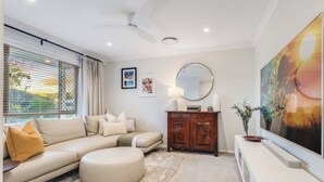A modern living room with a sectional sofa, a round ottoman, a wooden cabinet, and a large painting on the wall. - Sandstone Point (SEQ) 4 bedroom house (Sandstone Point)
