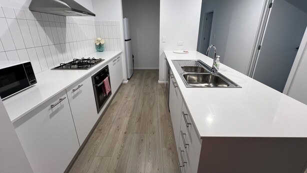 A modern kitchen with white cabinetry, a stainless steel sink, and a built-in oven. - Sandstone Point (SEQ) 4 bedroom house (Sandstone Point)