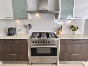 Una cocina moderna con estufa de acero inoxidable, dos armarios marrón oscuro, cafetera y bloque de cuchillos.