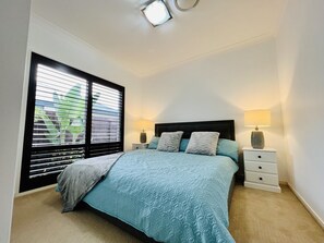 Un dormitorio con una cama, dos mesitas de noche, una ventana con persianas y una lámpara en el techo.