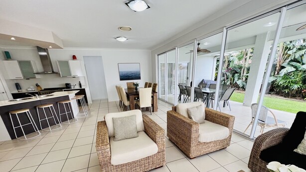 A modern kitchen with a dining area, wicker furniture, and a view of the garden through large glass doors.
