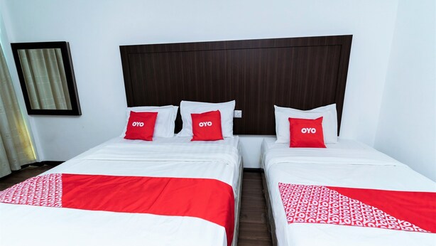 Habitació d'hotel amb dos llits, cadascun amb roba de llit blanca i detalls vermells, i un capçal de llit de fusta fosca.