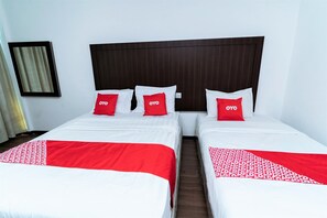 Une chambre d’hôtel avec deux lits, chacun doté de draps blancs et de touches de couleur rouge, ainsi que d’une tête de lit en bois foncé.