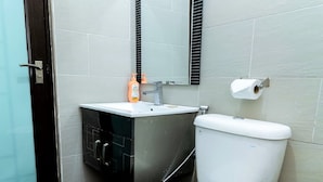 Un bany modern amb un vàter blanc, un lavabo amb un mirall a sobre i una zona de dutxa.