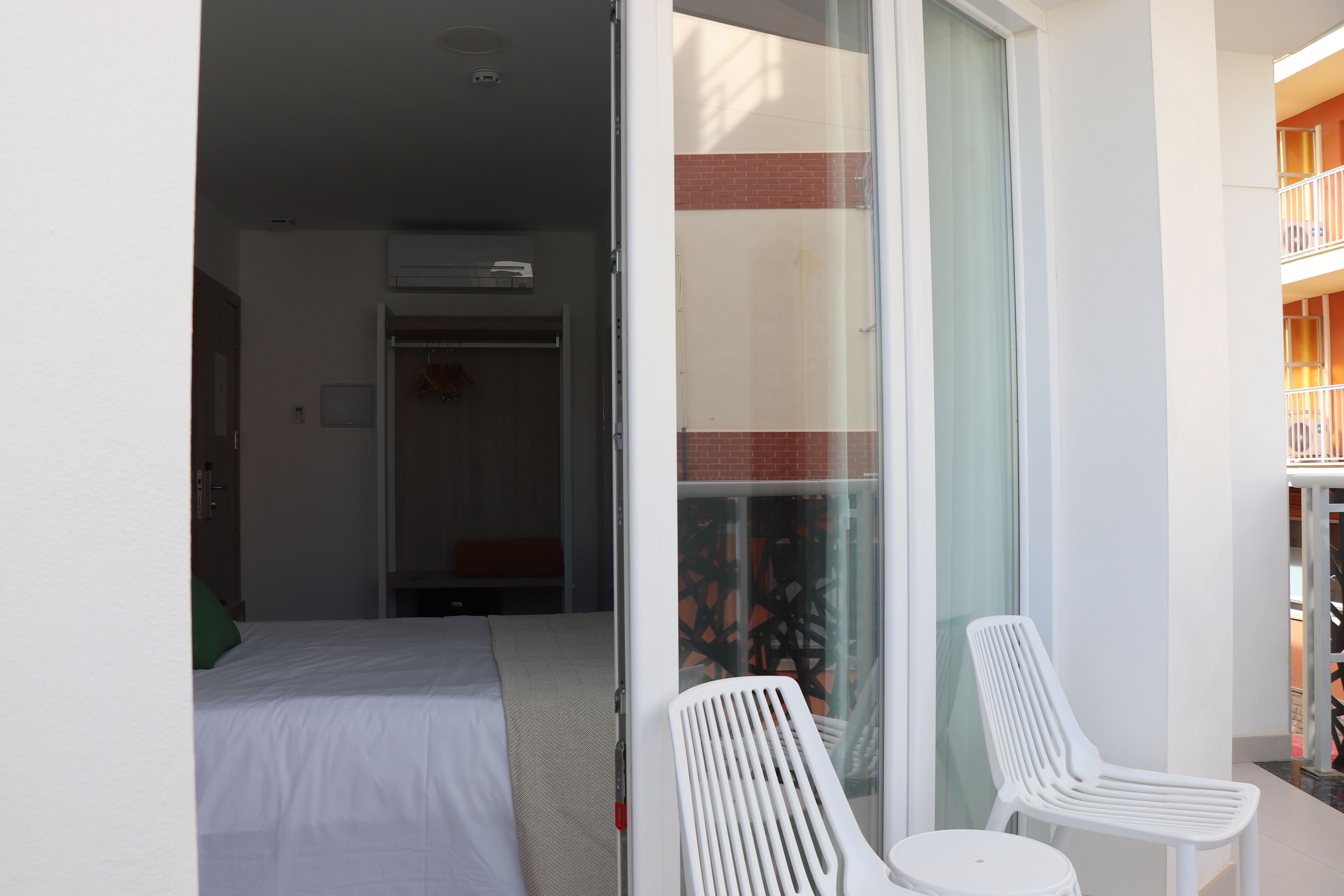 Habitación de hotel con cama, puerta corrediza de vidrio que da a un balcón con dos sillas blancas y una mesita.