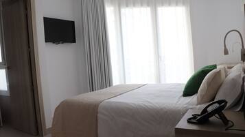 Habitación de hotel con cama, teléfono en la mesita de noche, televisor en la pared y ventana con cortinas.