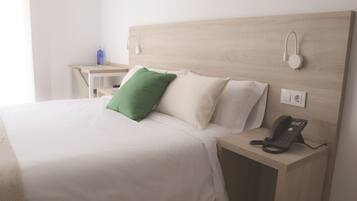 A neatly made bed with white bedding and a green pillow, a bedside table with a telephone, and a wall-mounted light fixture.