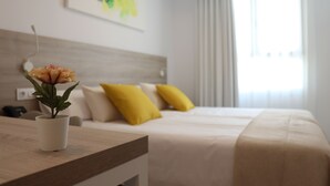 Une chambre d’hôtel avec un lit, une table de chevet ornée d’une plante en pot et une fenêtre avec des rideaux.