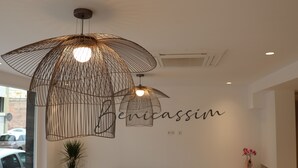 Un intérieur moderne avec un luminaire suspendu en forme de structure filaire, un canapé, une petite table avec un vase et un mur sur lequel est écrit le mot « Benicassim ».