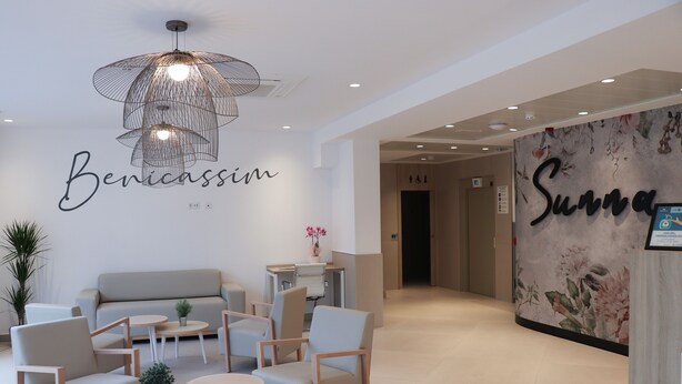 Un espace d’accueil moderne, aménagé avec un canapé, des fauteuils, des tables et un mur décoratif orné de motifs floraux.