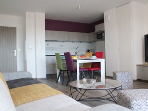 Uma sala de estar moderna com sofá, mesa de centro e área de refeições com cadeiras coloridas e uma mesa branca.