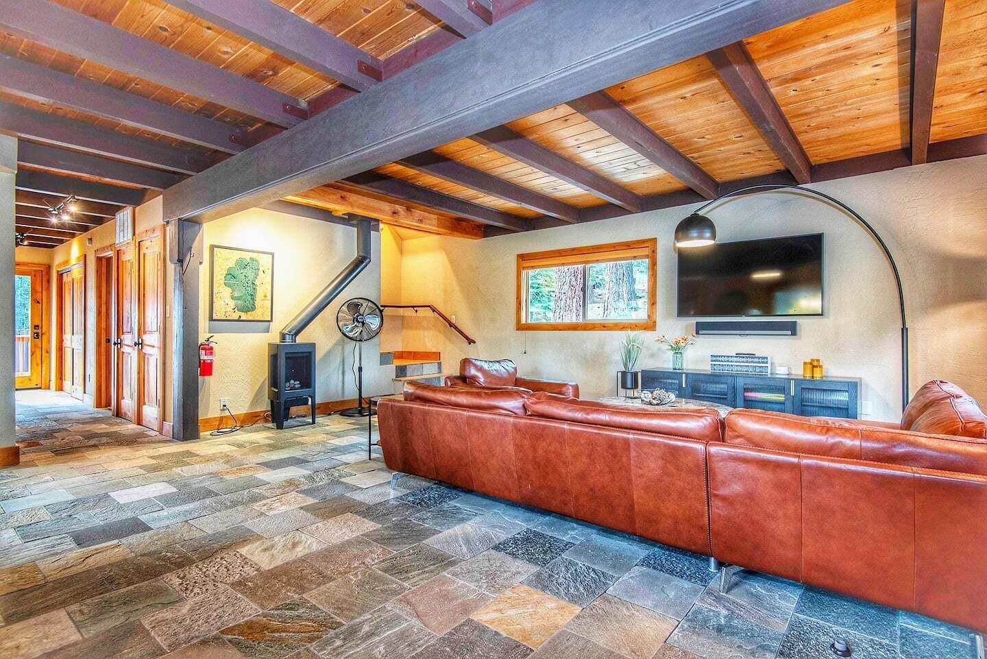 A spacious living room with a large leather sofa, a fireplace, a television, and a stone-tiled floor.