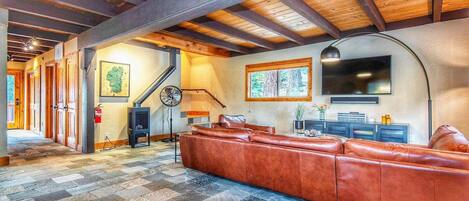 A spacious living room with a large leather sofa, a fireplace, a television, and a stone-tiled floor.