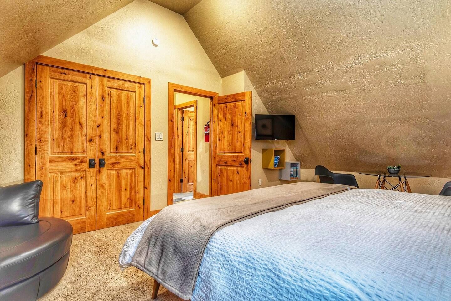 A bedroom with a large bed, wooden wardrobes, a television, and a small table with a bowl.