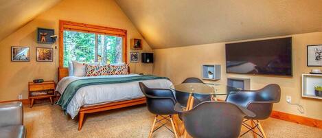 A cozy bedroom with a sloped ceiling, a large bed, a glass dining table, and modern chairs.