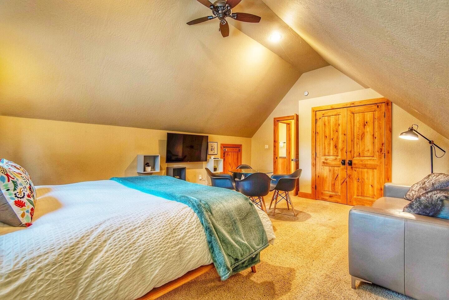 Un dormitorio con cama, escritorio, silla, ventilador de techo y puertas de madera.
