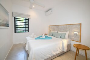 A hotel room with a bed, a small table, a window with blinds, and a ceiling fan. - Modern White and Blue on the Beach with a Pool (Poste Lafayette)