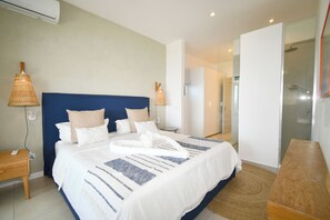A modern hotel room with a large bed, bedside lamps, a wooden nightstand, and a glass shower area.