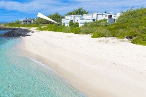 A beachfront property with a sandy beach, clear turquoise waters, and a modern building with multiple levels and balconies. - Modern White and Blue on the beach with pool (Poste Lafayette)
