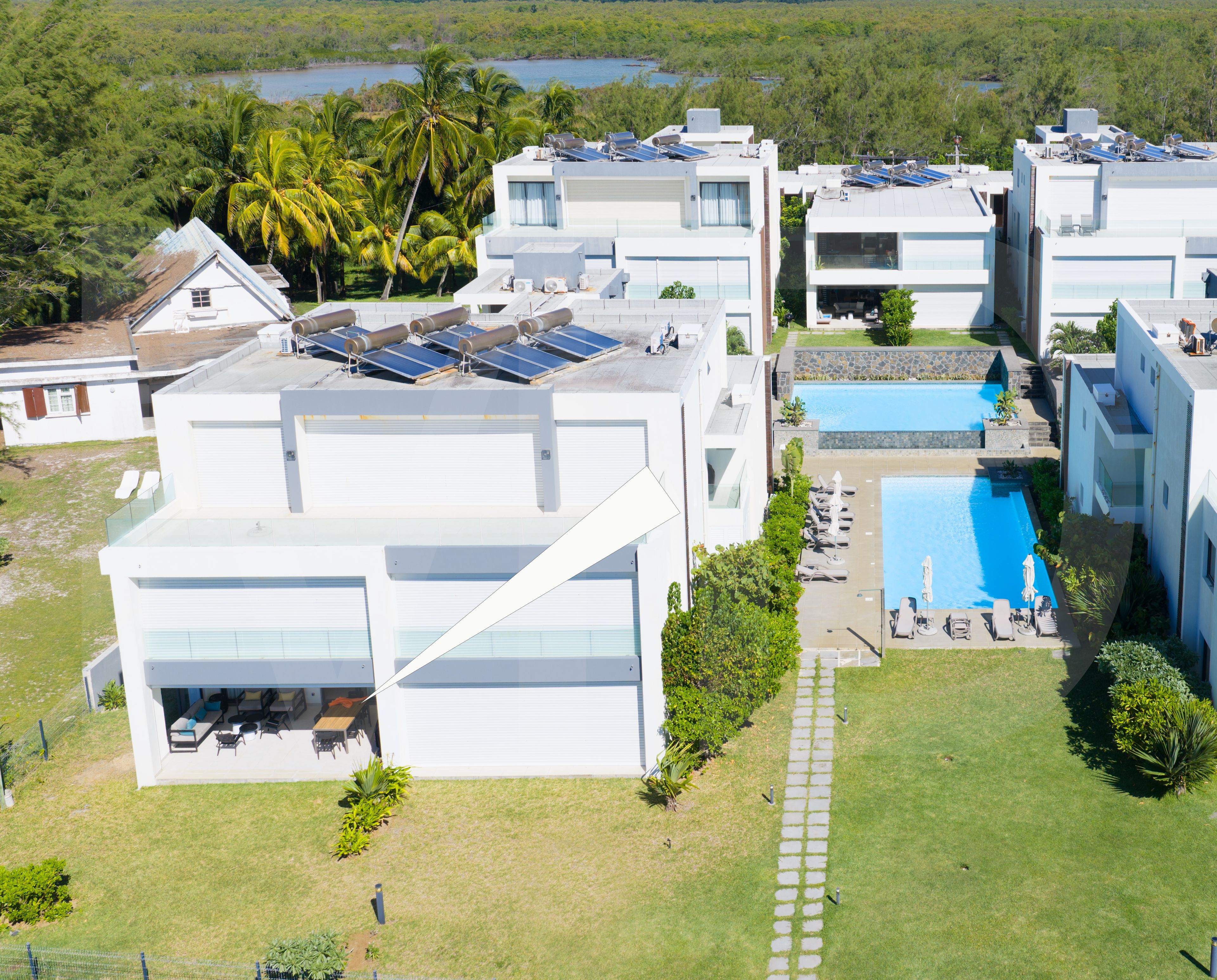 Un complejo residencial moderno con varios edificios, paneles solares, una piscina y un césped bien cuidado.