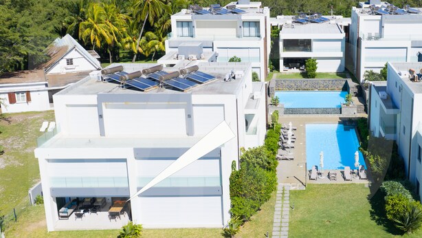 Um complexo residencial moderno com vários edifícios, painéis solares, piscina e um gramado bem cuidado.