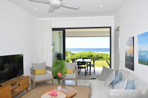 A modern living room with a television, sofa, and coffee table. There is a view of the ocean through a glass door. - Modern White and Blue on the beach with pool (Poste Lafayette)