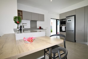 A modern kitchen with a wooden dining table, a refrigerator, and a built-in oven. - Modern White and Blue on the Beach with a Pool (Poste Lafayette)