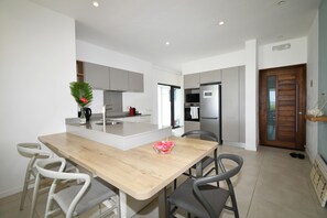 A modern kitchen with a central island, white cabinets, and a stainless steel refrigerator. - Modern White and Blue on the Beach with a Pool (Poste Lafayette)