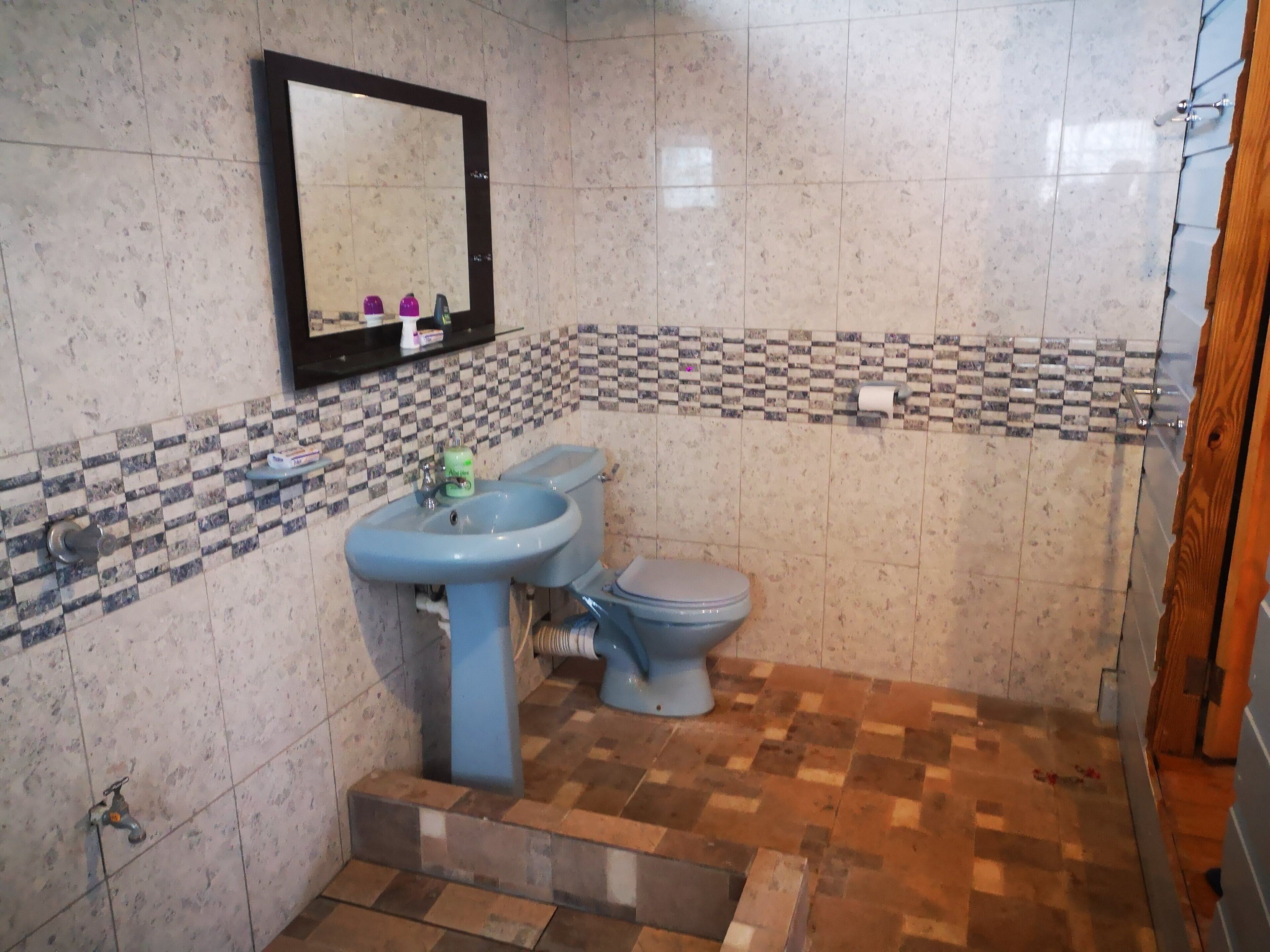 A bathroom with a sink, toilet, and mirror. The floor has a checkered pattern, and the walls have a tiled backsplash.