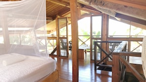 Een houten bed met klamboe in een kamer met houten vloeren en grote ramen.
