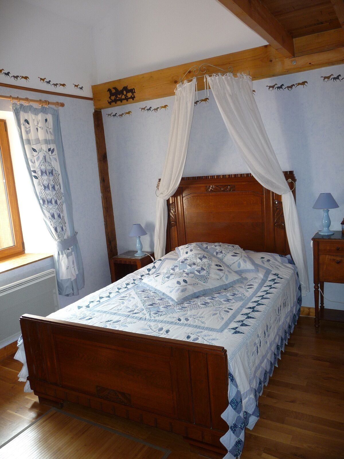 A wooden four-poster bed with a white canopy, a patterned bedspread, and a nightstand with a lamp.