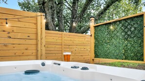 Un jacuzzi con una terraza de madera y un seto verde al fondo.
