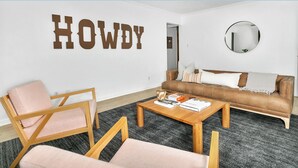 Una sala de estar moderna con un sofá de cuero marrón, dos sillas de madera, una mesa de centro con libros y un espejo montado en la pared.