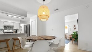 Una cocina moderna con armarios blancos, un refrigerador de acero inoxidable y una mesa de comedor de madera con sillas blancas.