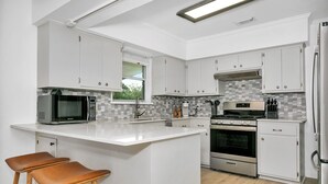 Una cocina moderna con armarios blancos, una isla central, microondas, estufa y refrigerador.