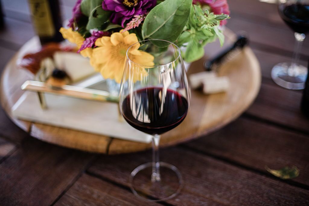 A wine glass with red wine on a wooden tray with a bouquet of flowers.
