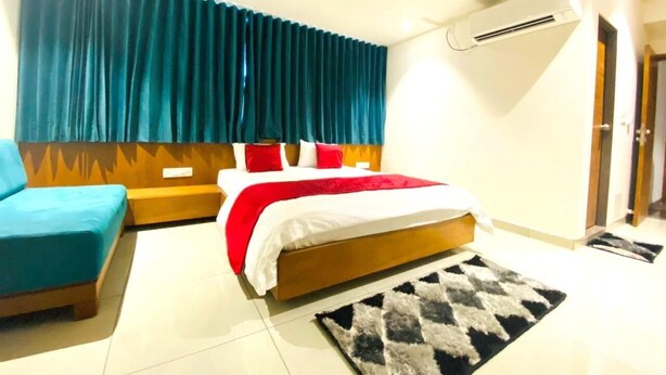 A hotel room with a bed, a sofa, a rug, and an air conditioning unit. - Hotel Prime (Gandhinagar)