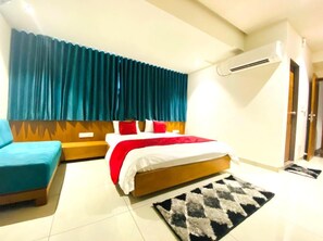 A hotel room with a bed, a sofa, a rug, and an air conditioning unit. - Hotel Prime (Gandhinagar)