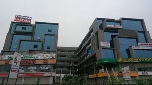 A multi-story commercial building with various storefronts, including signs for 'Pramukh Masrani' and 'Dakshination'. - Hotel Prime (Gandhinagar)