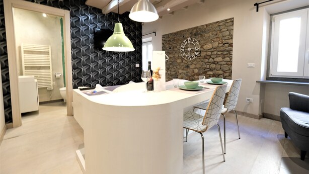 A modern kitchen with a central island, pendant lighting, and a stone accent wall. - Wine Apartments Florence Grechetto (Florence)