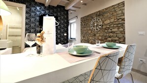A dining area with a stone wall, a clock, and a table set with a green bowl and wine glasses. - Wine Apartments Florence Grechetto (Florence)