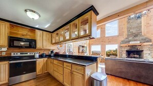 Une cuisine avec des meubles en bois, une cuisinière en acier inoxydable, un four à micro-ondes et une cheminée en pierre.