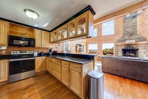 A kitchen with wooden cabinets, a stainless steel stove, a microwave, and a stone fireplace.