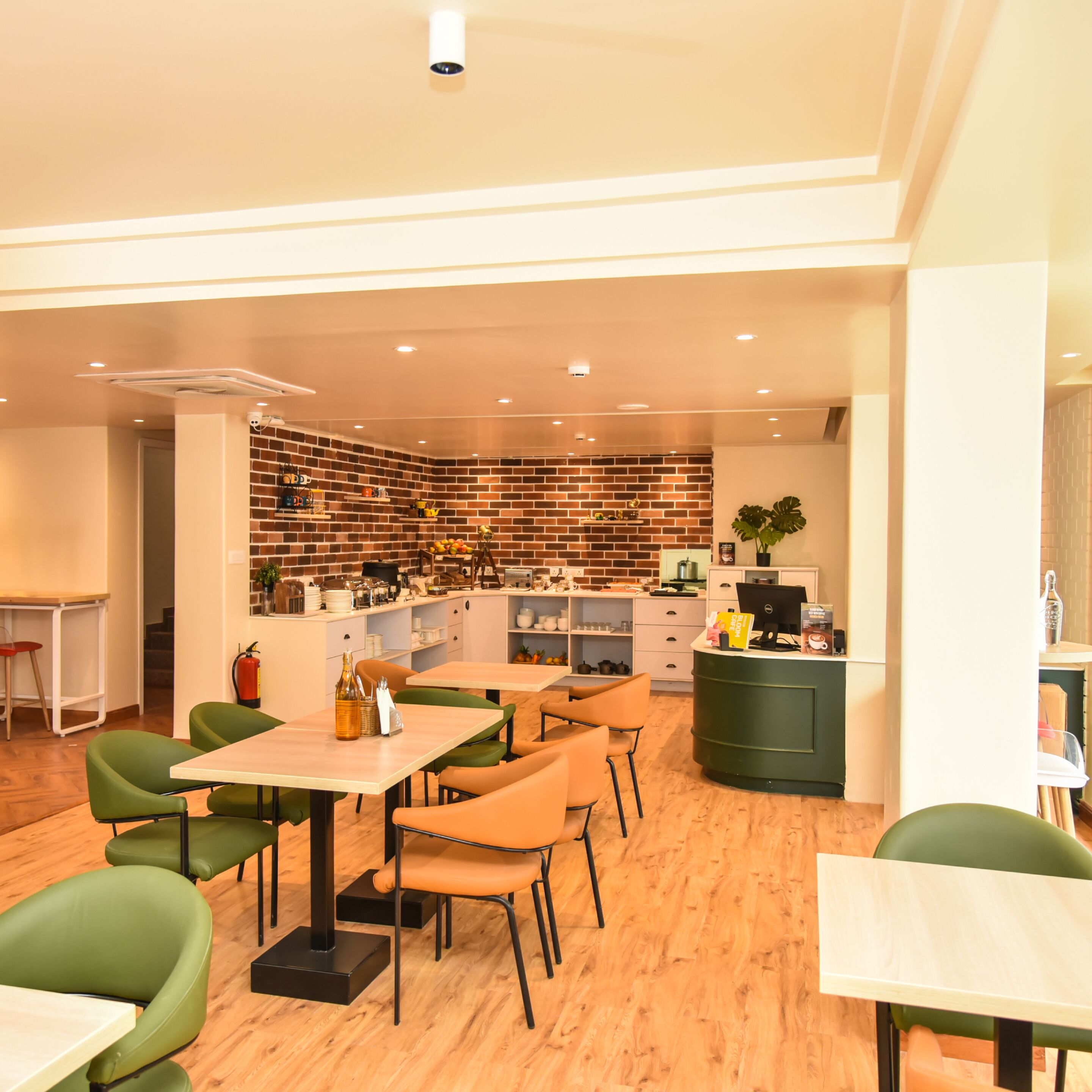 A modern restaurant with a brick wall backdrop, wooden flooring, and green and orange chairs.