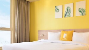 Habitación de hotel con una cama grande, cabecero de madera y vistas a la ciudad a través de un ventanal.