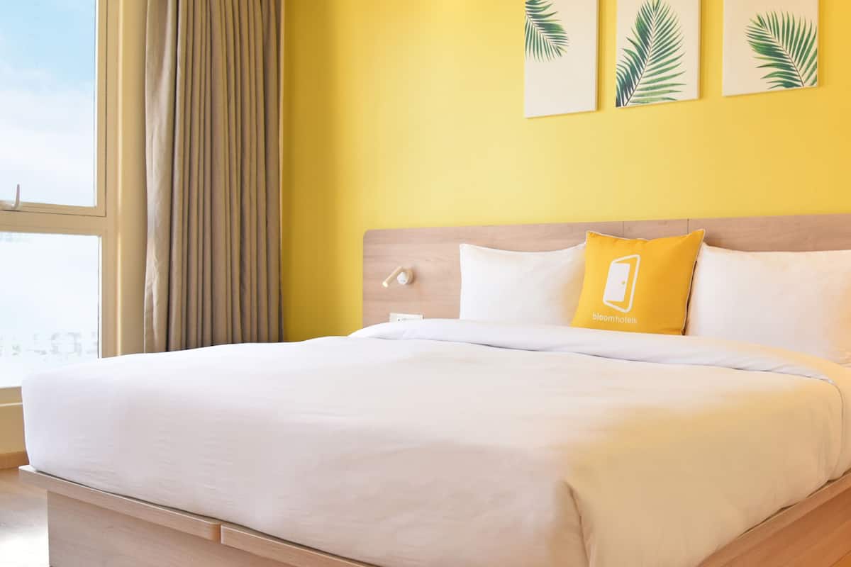 Habitación de hotel con una cama grande, cabecero de madera y vistas a la ciudad a través de un ventanal.