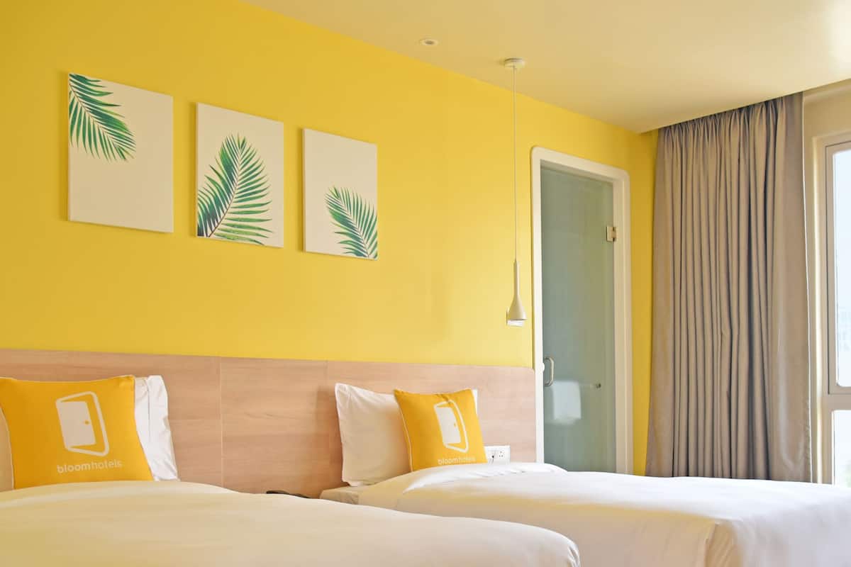 Habitación de hotel con dos camas, paredes amarillas y una ventana con cortinas.