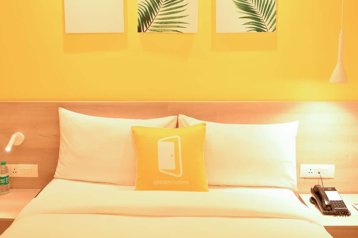 Habitación de hotel con una cama, una mesita de noche con lámpara, un teléfono y una botella de agua. En la pared sobre la cama hay tres hojas enmarcadas.