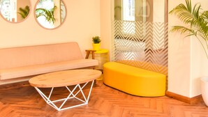 Un interior moderno con piso de madera, un sofá, un otomano amarillo y una mesa redonda.